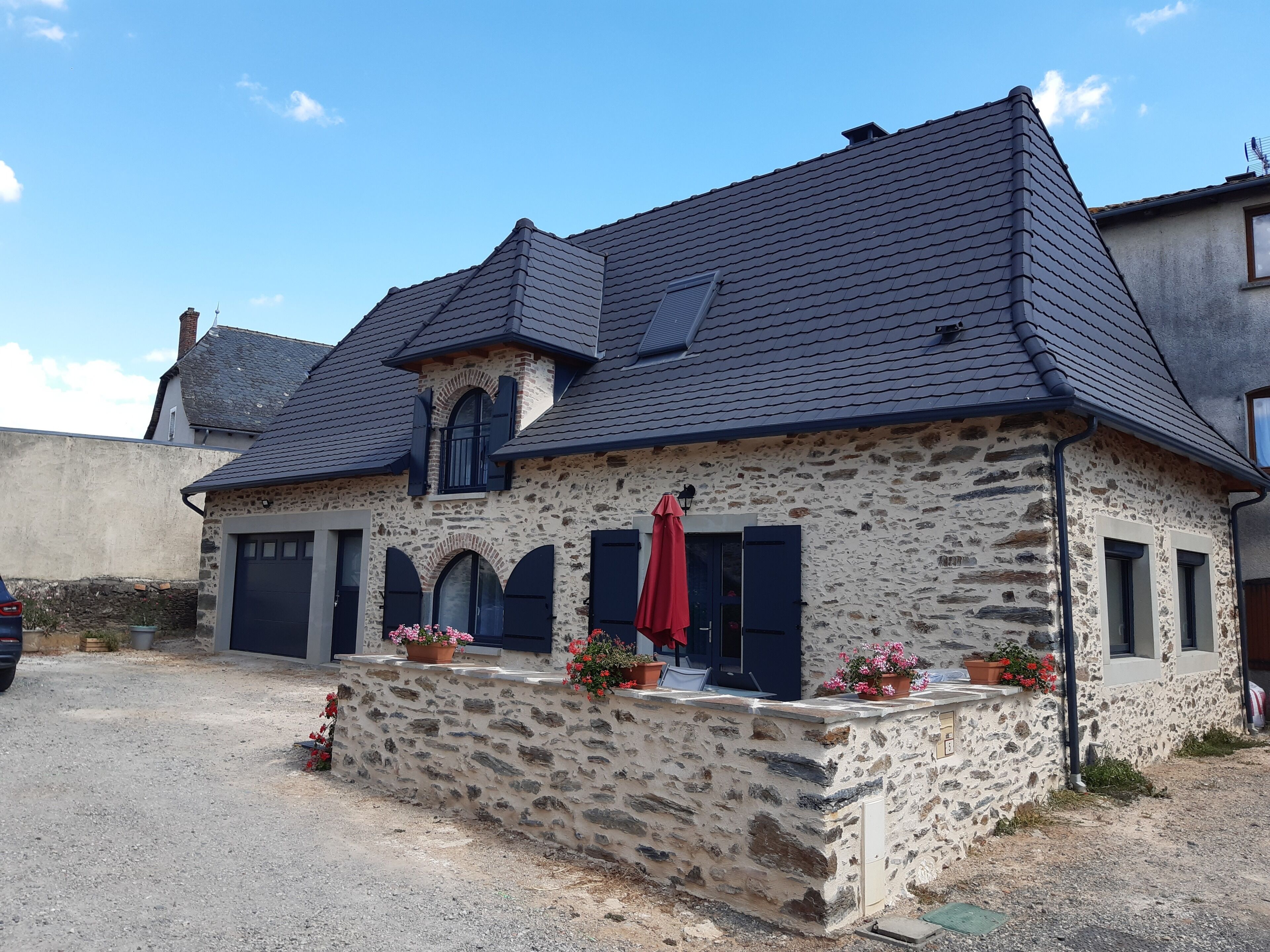 A stone house with a dark roof, multiple windows, and a red umbrella.