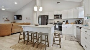 A modern kitchen with white cabinetry, a central island with stools, a built-in oven, and a microwave.