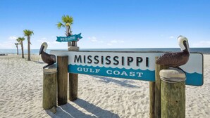 A wooden sign with 'MISSISSIPPI GULF COAST' and a 'welcome' sign, with pelicans on posts.