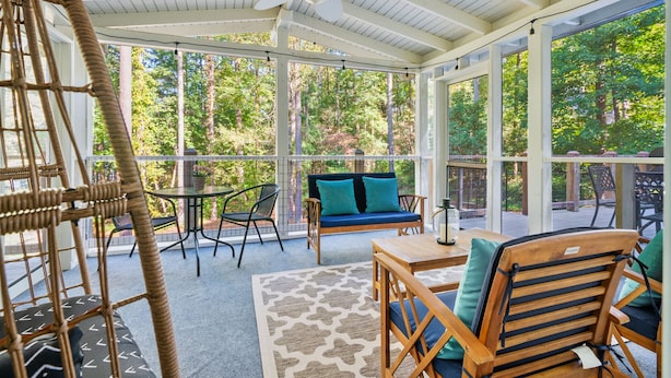 A covered patio area with a ceiling fan, wicker furniture, a blue sofa, and a patterned rug.