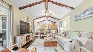 A spacious living room with a high ceiling, wooden beams, a large flat-screen TV, a sofa, and a coffee table.