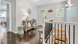A hallway with a wooden floor, a white door with a green glass panel, a small table with a lamp, and a staircase with black railings.
