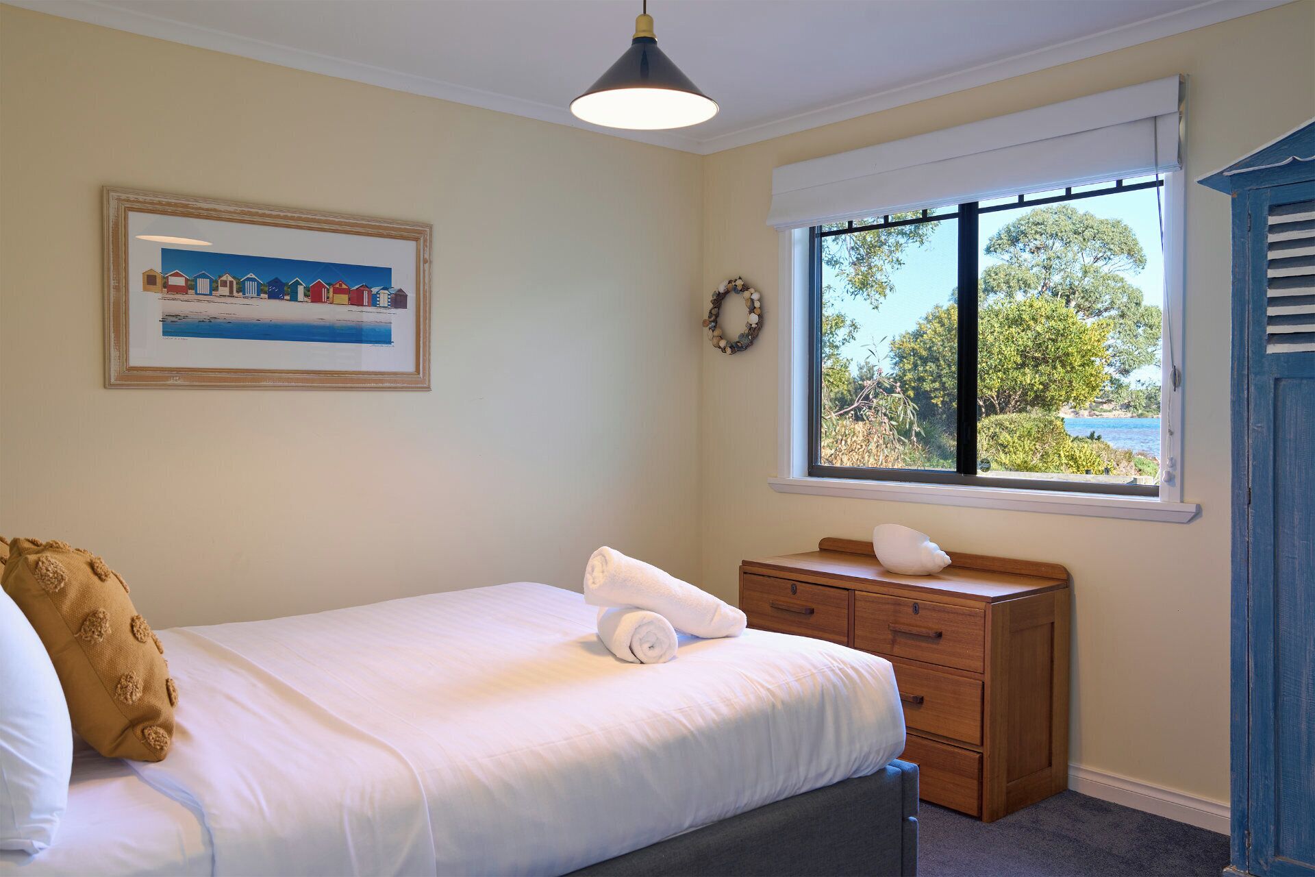 Ein Schlafzimmer mit Bett, Kommode, Fenster mit Blick und einem gerahmten Bild an der Wand.