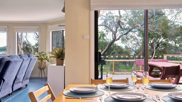 Zona pranzo con tavolo imbandito per quattro persone, una pianta in vaso e vista su un albero attraverso una finestra.