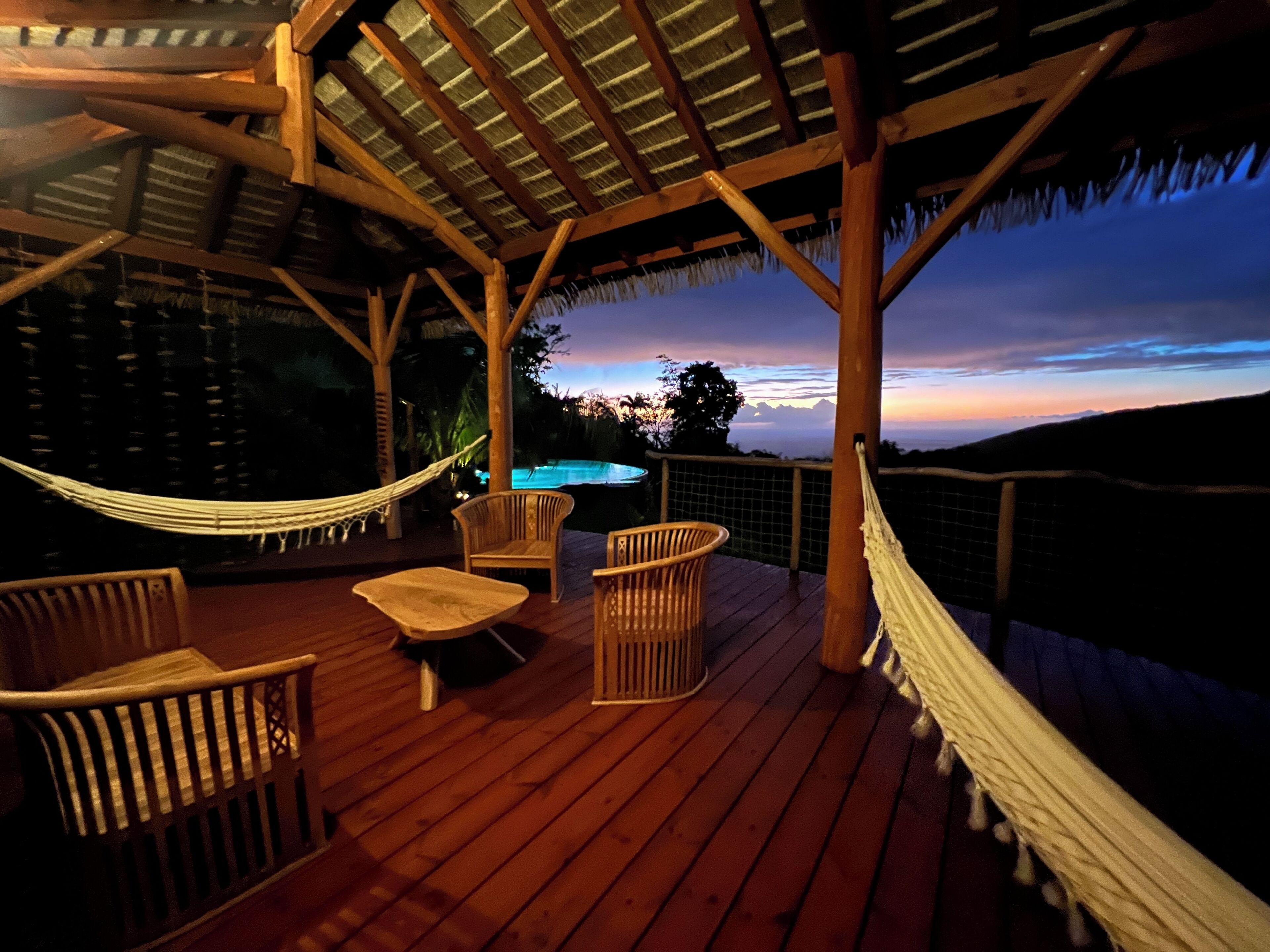 An outdoor wooden deck with a hammock, wicker chairs, and a pool in the background.