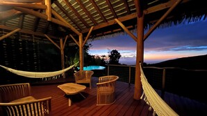 Eine Holzterrasse im Freien mit einer Hängematte, Korbstühlen und einem Pool im Hintergrund.