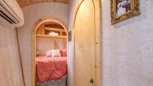 A cozy room with a wooden arched doorway leading to a bed with a red bedspread and a patterned skirted skirt. - ☆ Magical Gypsy Wagon ☆ Unique Mountain Getaway (Fairplay)