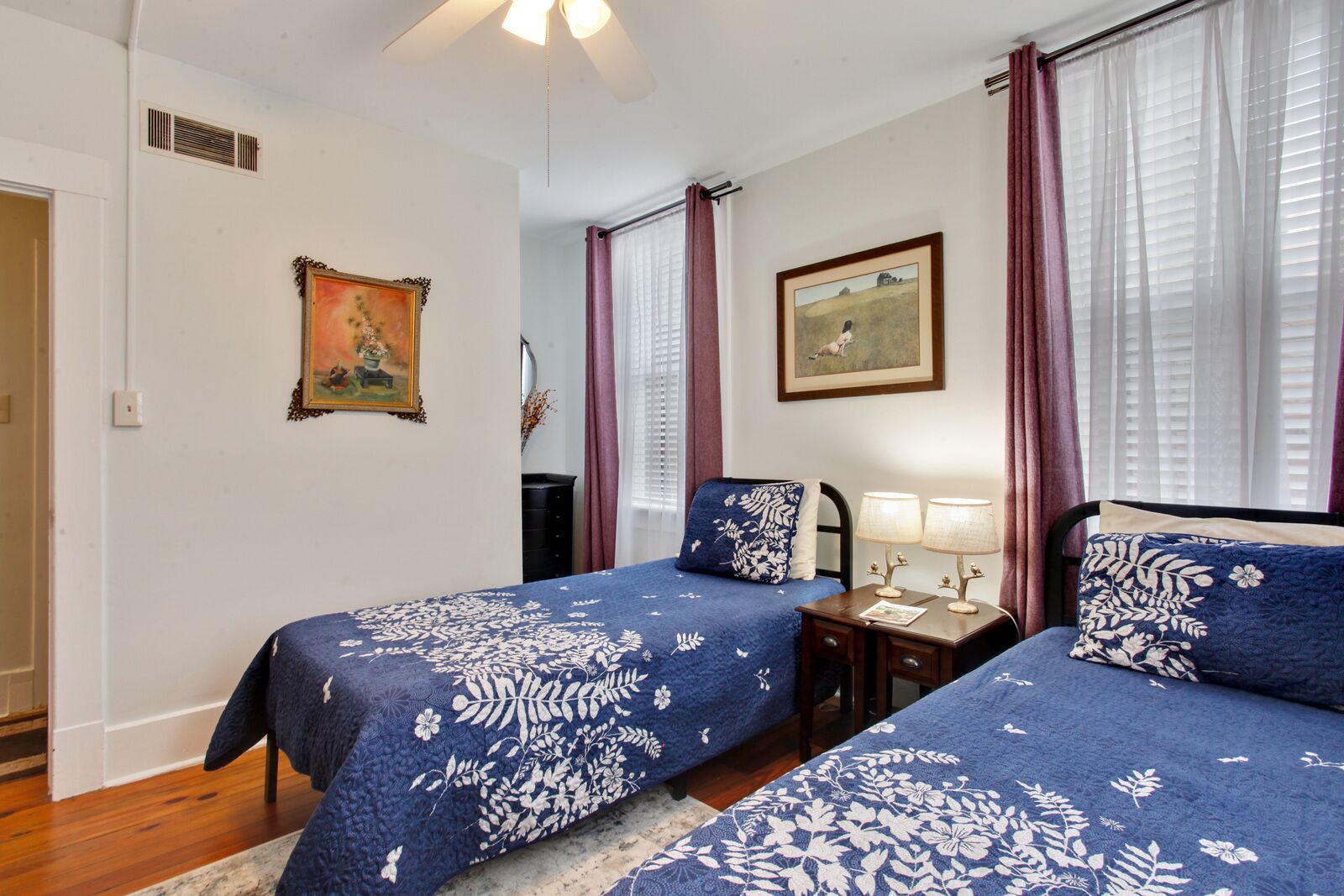 A bedroom with two beds, a nightstand, a lamp, and two framed pictures on the wall.