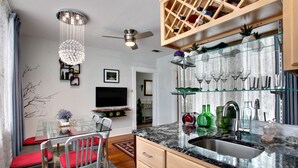 A modern kitchen with a marble countertop, a built-in wine rack, and a dining area with a glass table and chairs. - Lincoln St Condo: Quiet Spot Near Night Life! (Savannah)