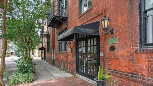 A brick building with a black awning, a green sign, and a potted plant on the sidewalk. - Lincoln St Condo: Quiet Spot Near Night Life! (Savannah)