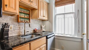 A kitchen with wooden cabinets, a granite countertop, a built-in spice rack, and a window with blinds. - Lincoln St Condo: Quiet Spot Near Night Life! (Savannah)