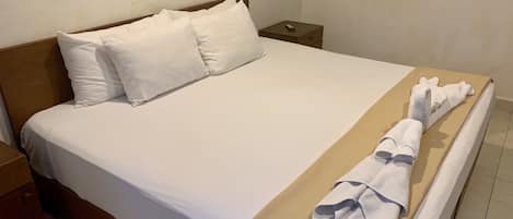 A neatly made bed with white linens and a beige blanket, a wooden headboard, and a small bedside table with a remote control.