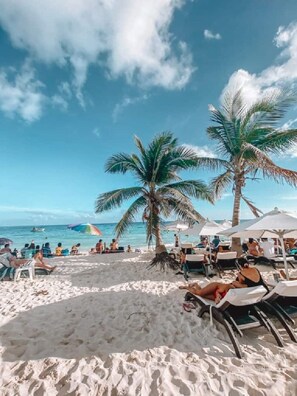 A beach with palm trees, sun loungers, and umbrellas.