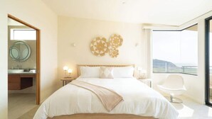 A modern hotel room with a large bed, a view of the sea, and a balcony with a white chair.