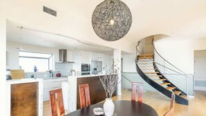 A spacious kitchen with a central island, a dining area with a round table, and a curved staircase.