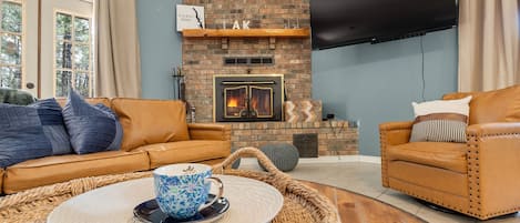 Una sala de estar con chimenea de ladrillo, sofás de cuero, un televisor de pantalla plana y un ventanal con cortinas.