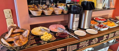 Un bufé de desayuno con diversos alimentos, cafeteras y un tapete decorativo.