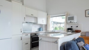 A modern kitchen with white cabinetry, stainless steel appliances, a window with curtains, and a view of the outside.