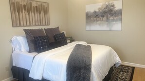 Un letto rifatto con lenzuola bianche, una coperta grigia e cuscini decorativi.