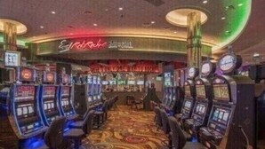 Un'area casinò con diverse slot machine, un neon sopra il bar e un tappeto decorato.