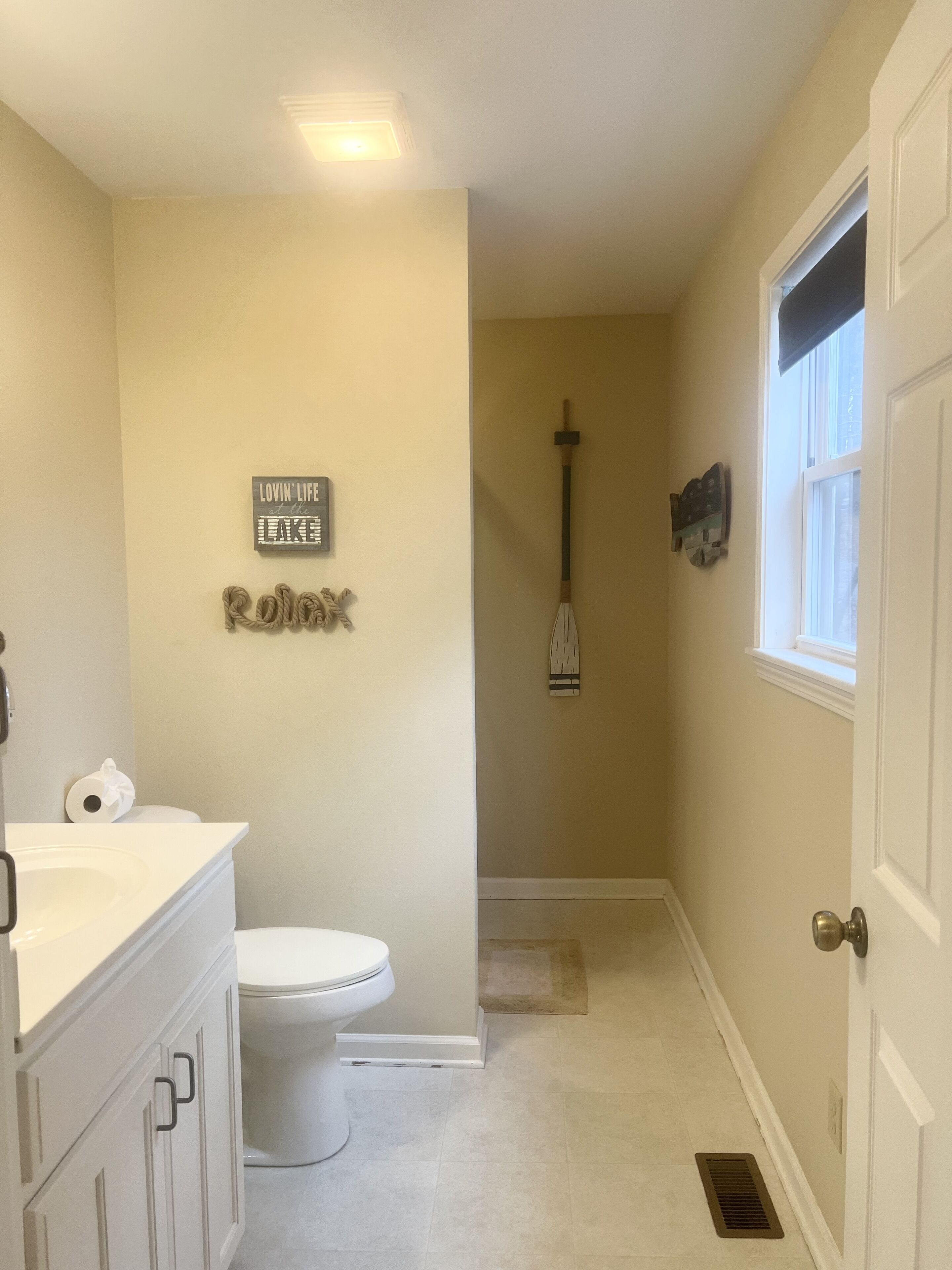 A bathroom with a toilet, a sink, and a shower area. There is a sign on the wall and a window with a view.