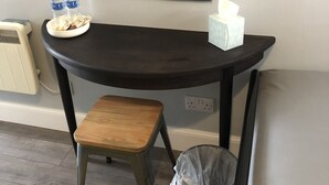 A small desk with a stool, a mirror, a tissue box, and a trash can.