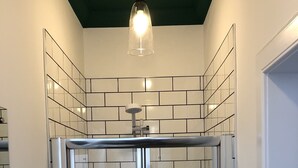 A modern bathroom with white subway tiles, a glass shower enclosure, a ceiling light fixture, and a small shelf with cups.