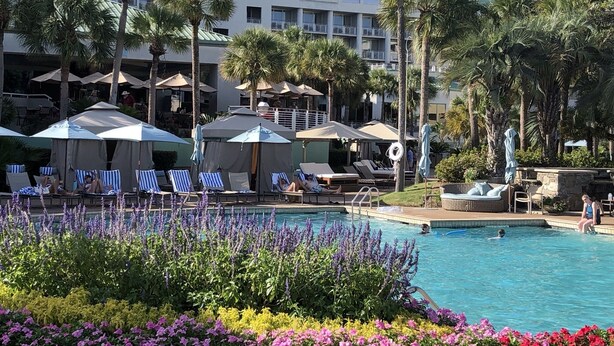 A hotel pool area with lounge chairs and umbrellas, surrounded by palm trees and flowers. - Beach Luxury Villa w/ Free Golf & Tennis plus Westin Resort Amenities! (Hilton Head Island)