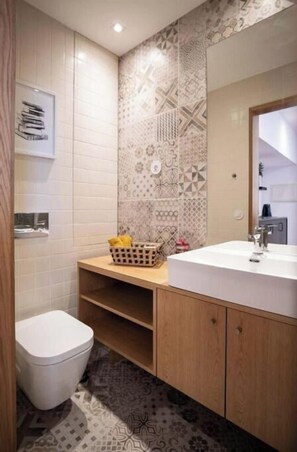 Bathroom features a white toilet, sink, and shower area with a geometric tile pattern on the walls.
