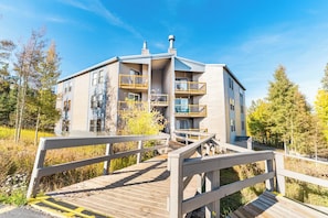Un immeuble à plusieurs étages doté de balcons, d’une terrasse en bois et entouré d’un cadre naturel.
