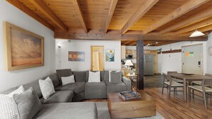 A cozy living room with a gray sectional sofa, wooden coffee table, and a dining area with a wooden table and chairs. - Treehouse #107, Building G by Summit County Mountain Retreats (Silverthorne)