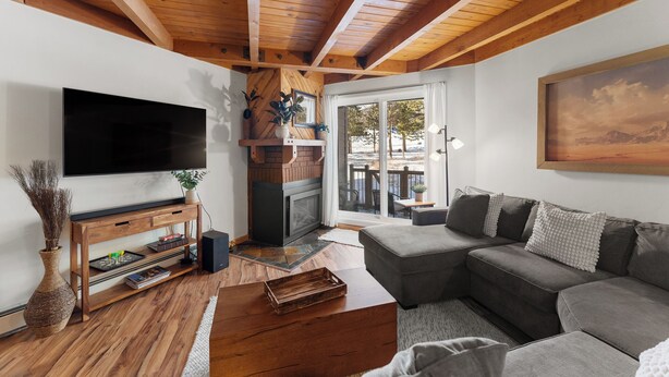 A modern living room with a fireplace, a large flat-screen TV, a sectional sofa, and a wooden ceiling. - Treehouse #107, Building G by Summit County Mountain Retreats (Silverthorne)