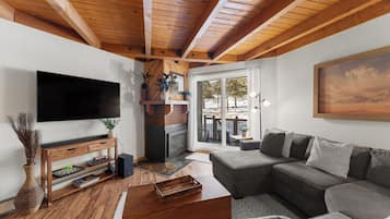 A modern living room with a fireplace, a large flat-screen TV, a sectional sofa, and a wooden ceiling.