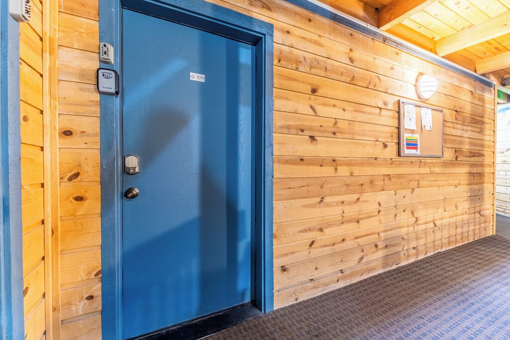 A blue door with a keypad lock, a wooden wall with a bulletin board, and a carpeted floor.