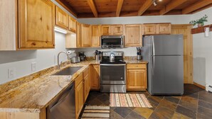 A kitchen with wooden cabinets, stainless steel appliances, granite countertops, and a tiled floor. - Treehouse #107, Building G by Summit County Mountain Retreats (Silverthorne)