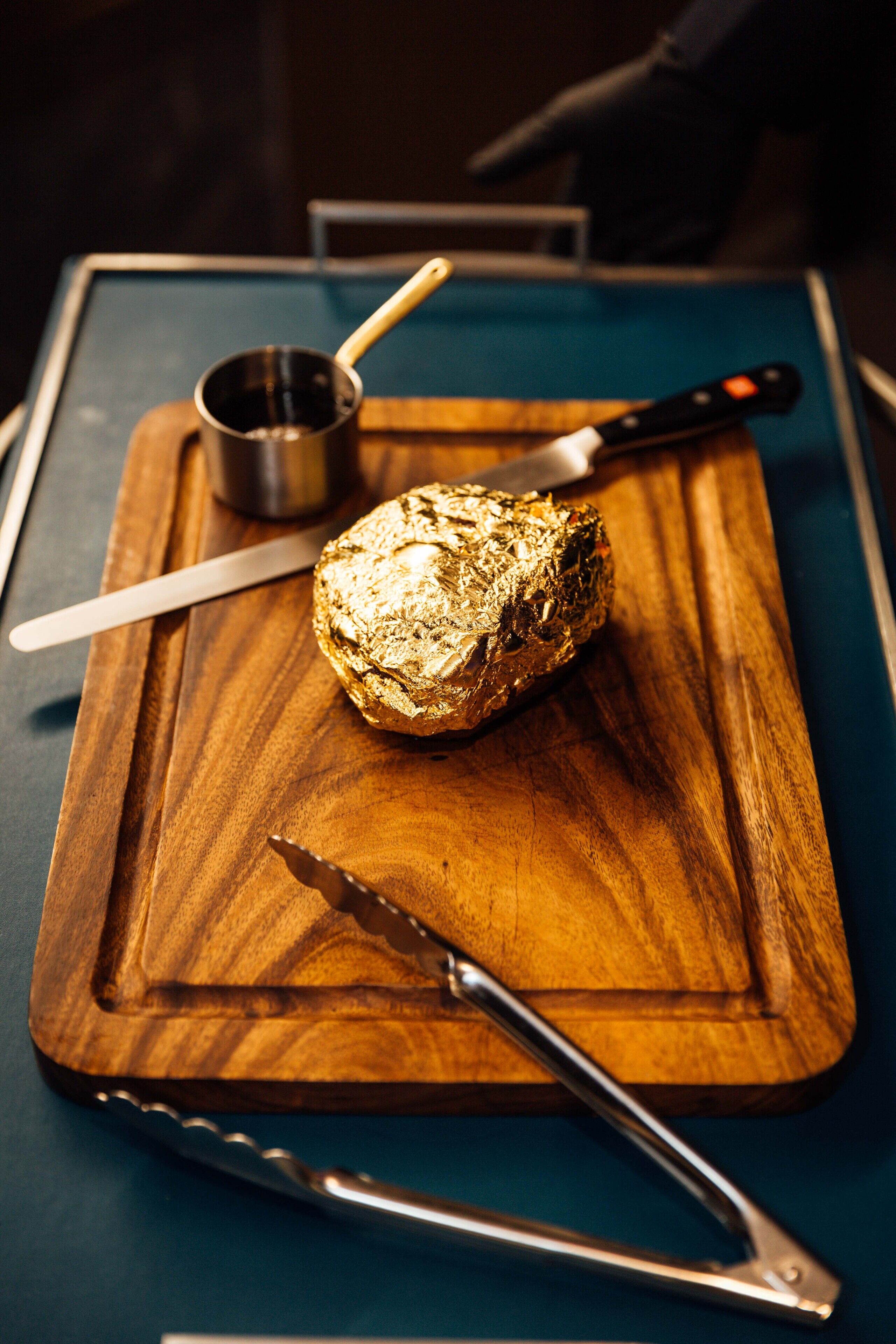 Un morceau d’aliments sur une planche à découper en bois, avec un couteau et un petit récipient en métal.
