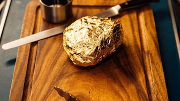 Un morceau d’aliments sur une planche à découper en bois, avec un couteau et un petit récipient en métal.