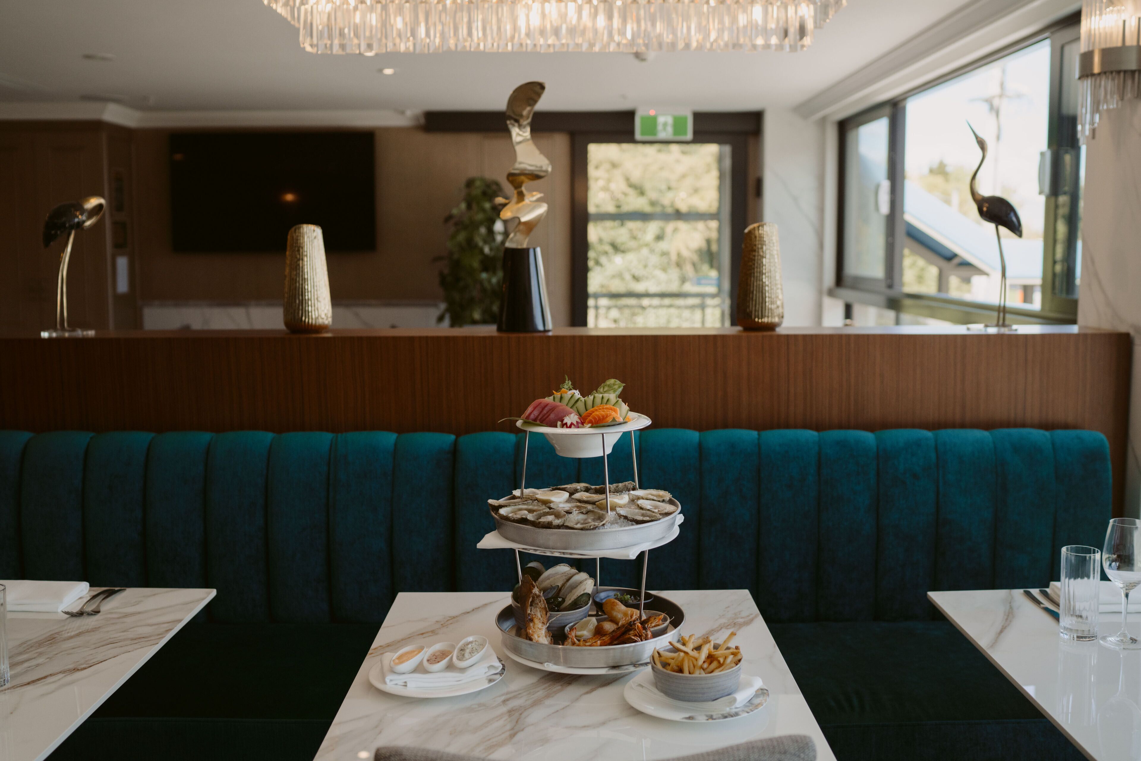 A dining area with a three-tiered dessert display, a marble table, and teal upholstered seating.