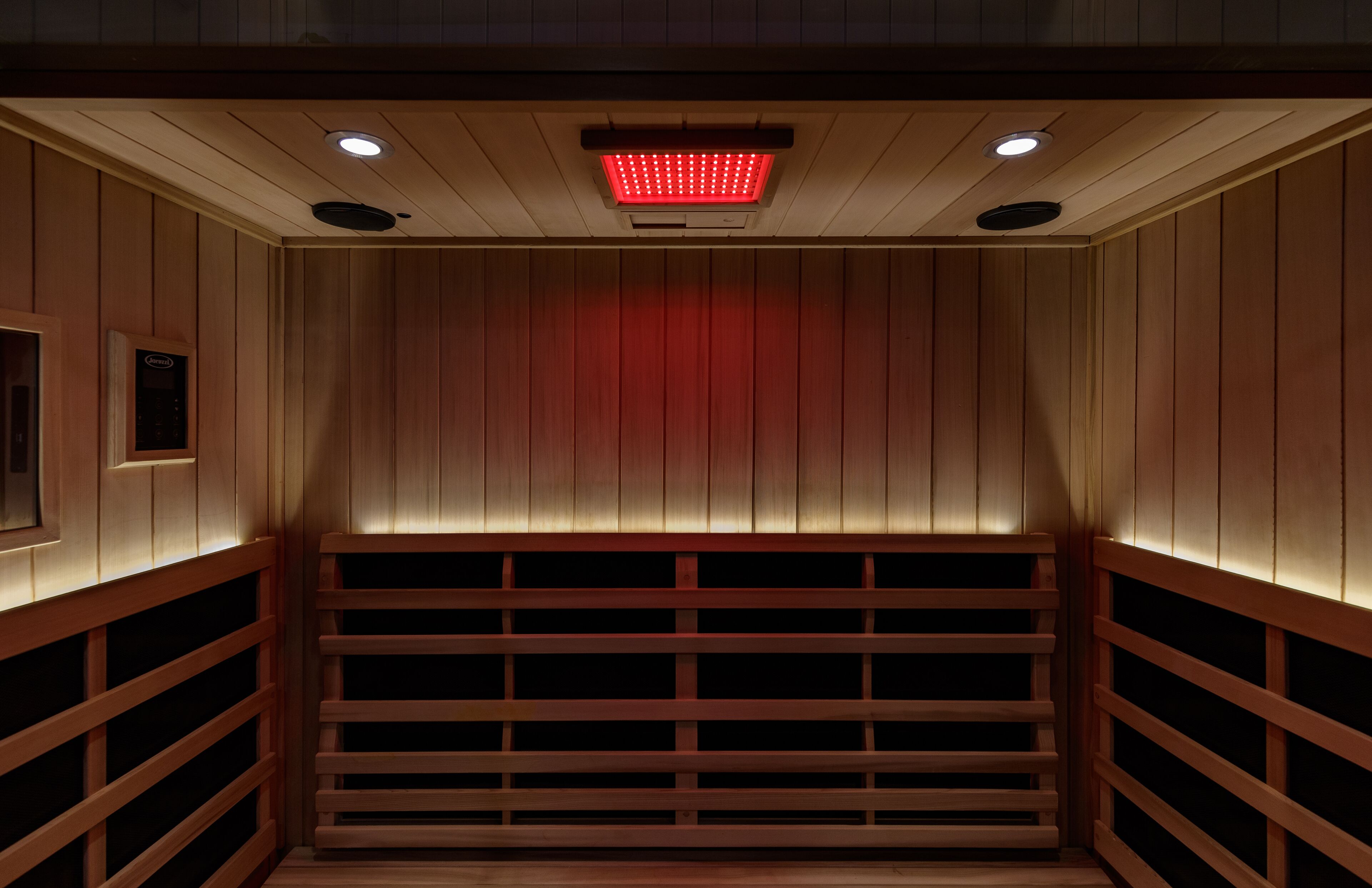 A sauna with wooden walls and benches, a ceiling light, and a control panel.