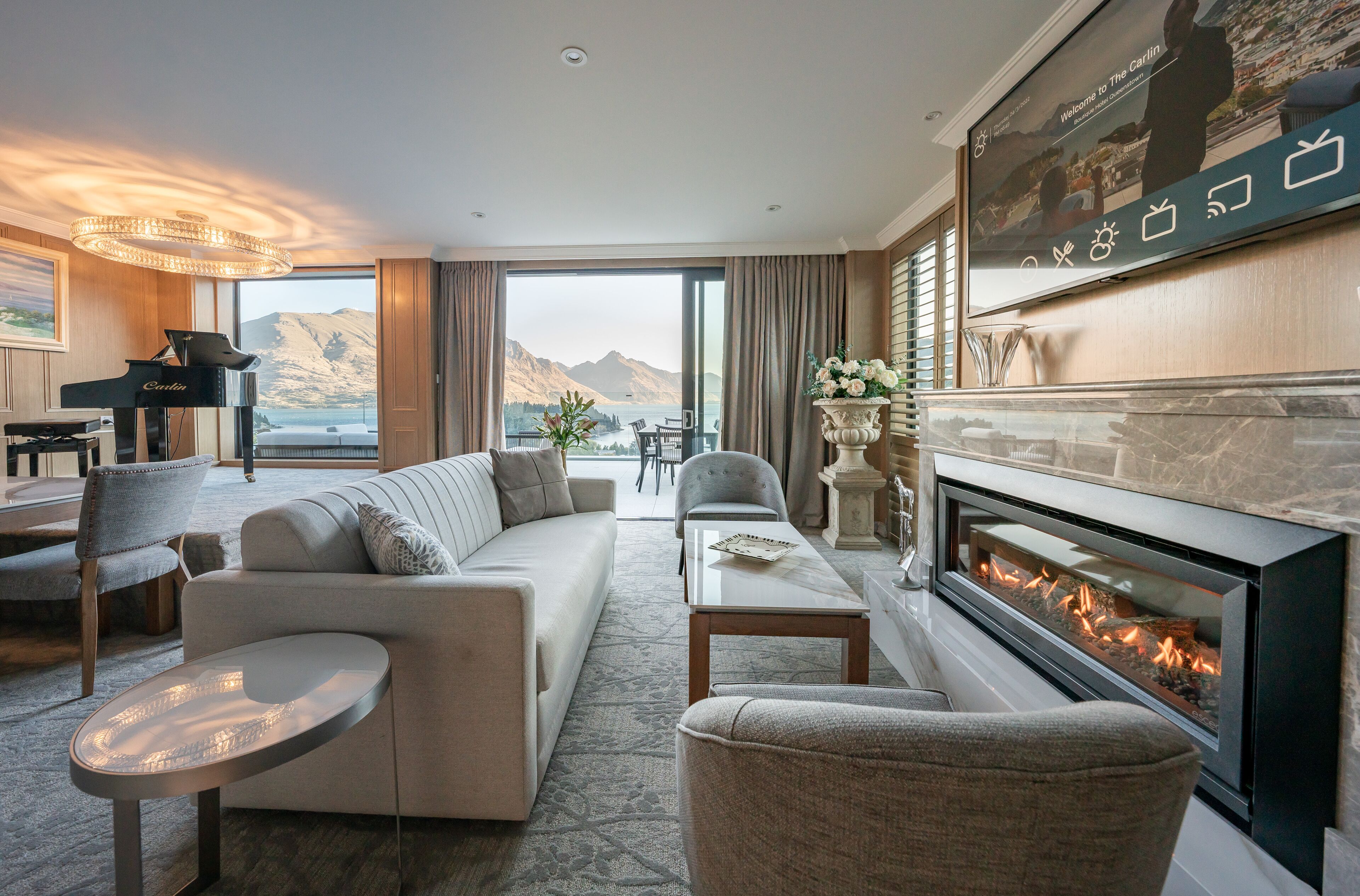 Una sala de estar moderna con un piano, un sofá, una chimenea y un amplio ventanal con vistas a un paisaje montañoso.