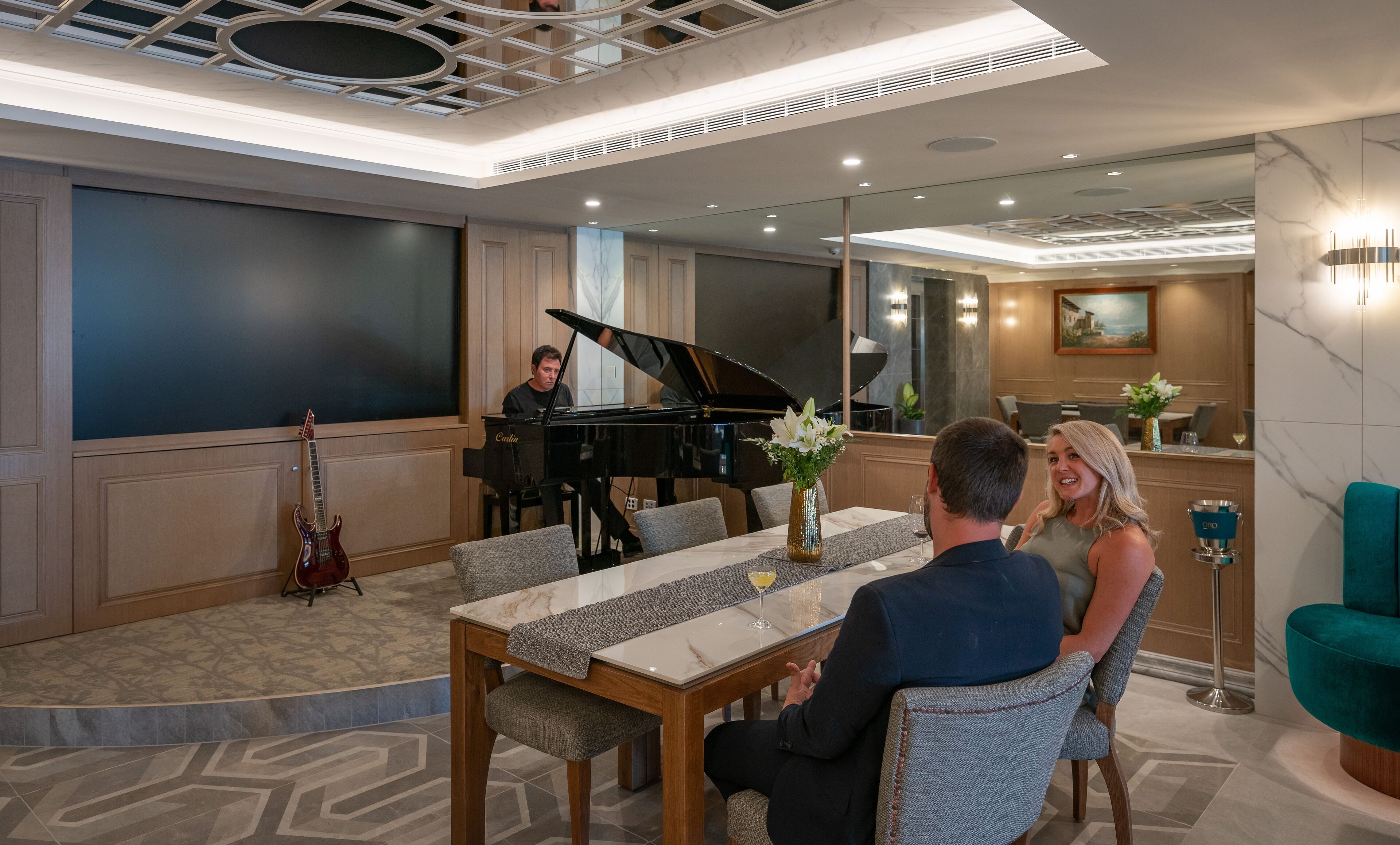 A modern hotel room with a piano, a dining table with chairs, and a large screen.