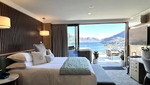 Une chambre d’hôtel avec un grand lit, un bureau, une chaise et une vue sur la mer et les montagnes.