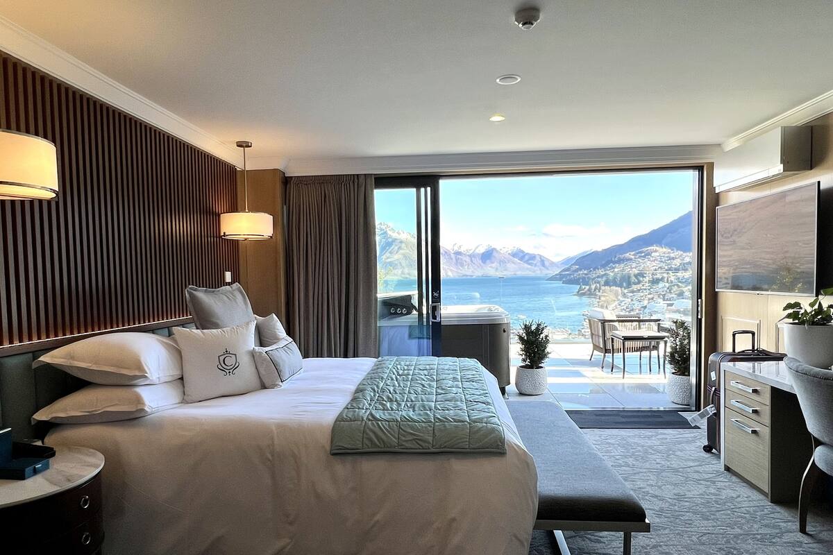 Een hotelkamer met een groot bed, een bureau, een stoel en uitzicht op zee en bergen.