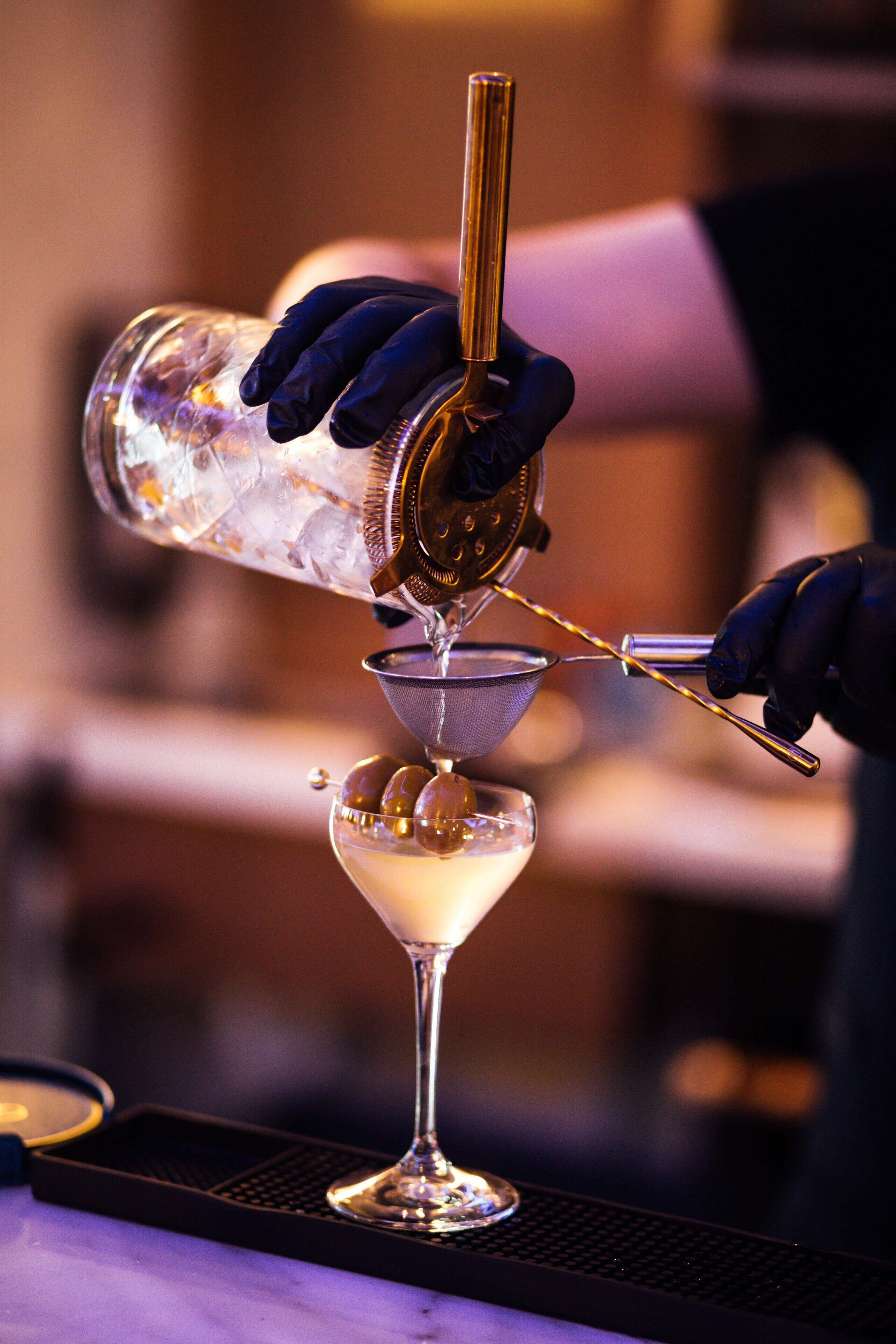 Un barman verse une boisson dans un verre à martini à l’aide d’un doseur et d’une passoire.