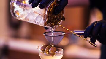 Un barman verse une boisson dans un verre à martini à l’aide d’un doseur et d’une passoire.