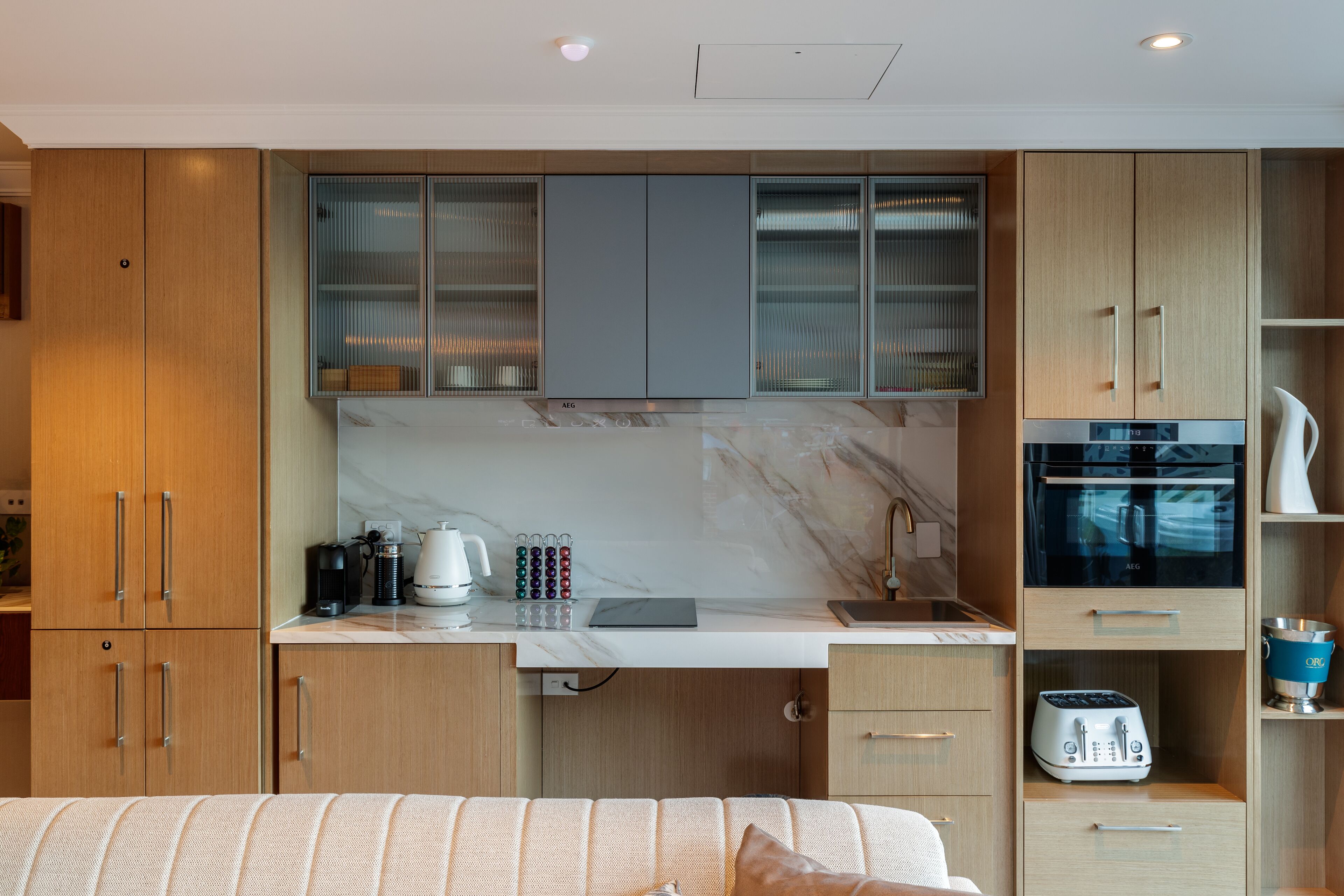A compact kitchen with wooden cabinets, a marble backsplash, and modern appliances including a coffee maker, toaster, and oven.