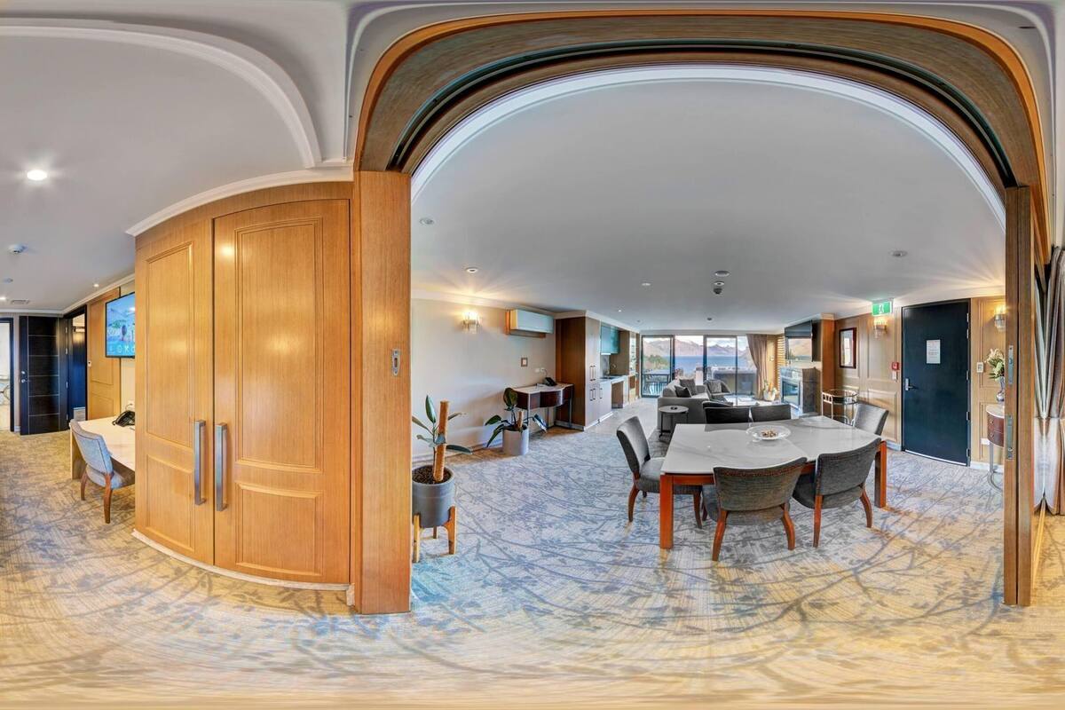 Een panoramisch uitzicht op een hotel lobby met een eetgedeelte, een receptiebalie en een slaapkamer met een groot bed en uitzicht op zee.