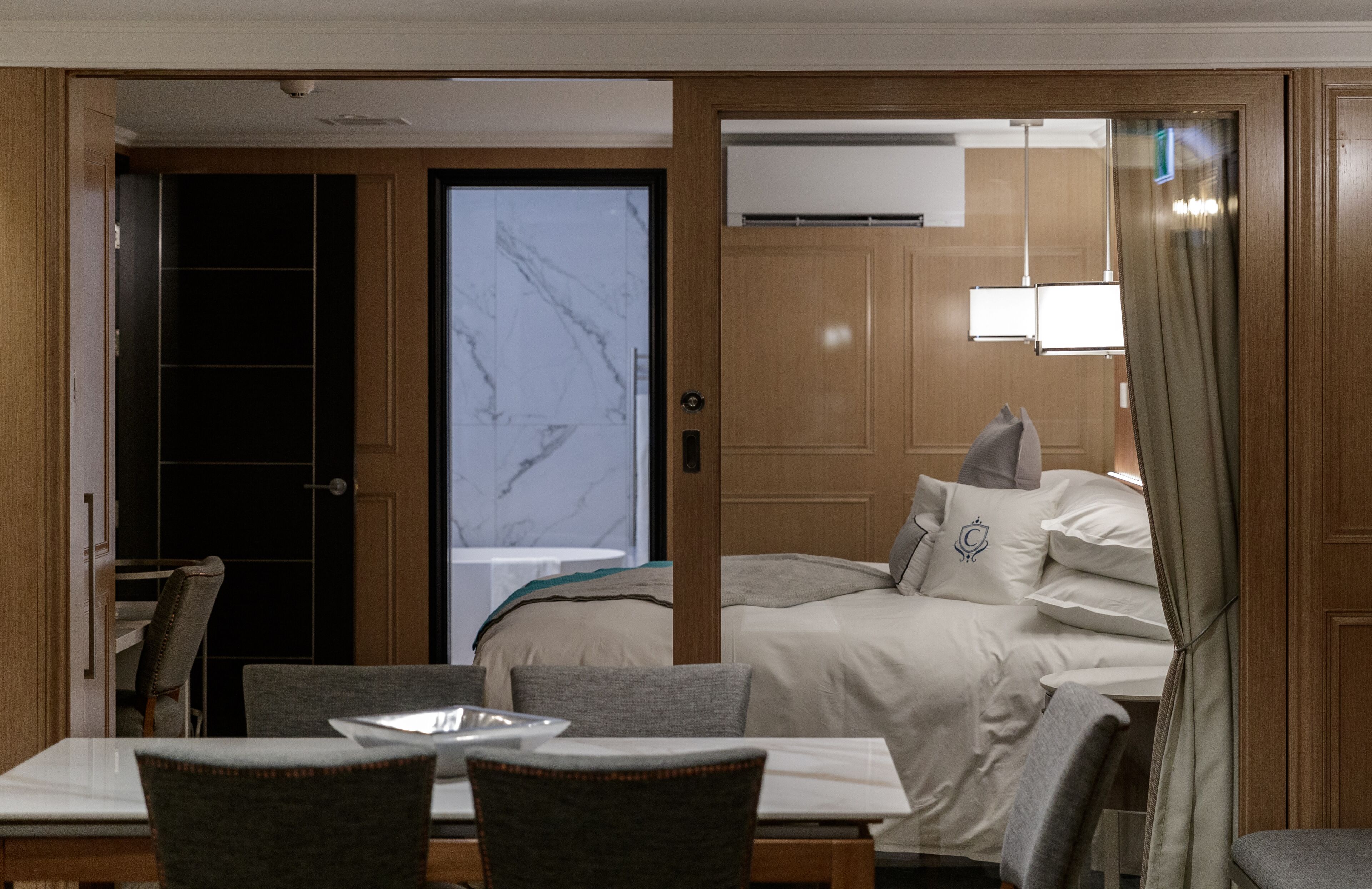 Une chambre d’hôtel avec un lit, une table à manger et des chaises, et une vue sur l’extérieur par une porte.