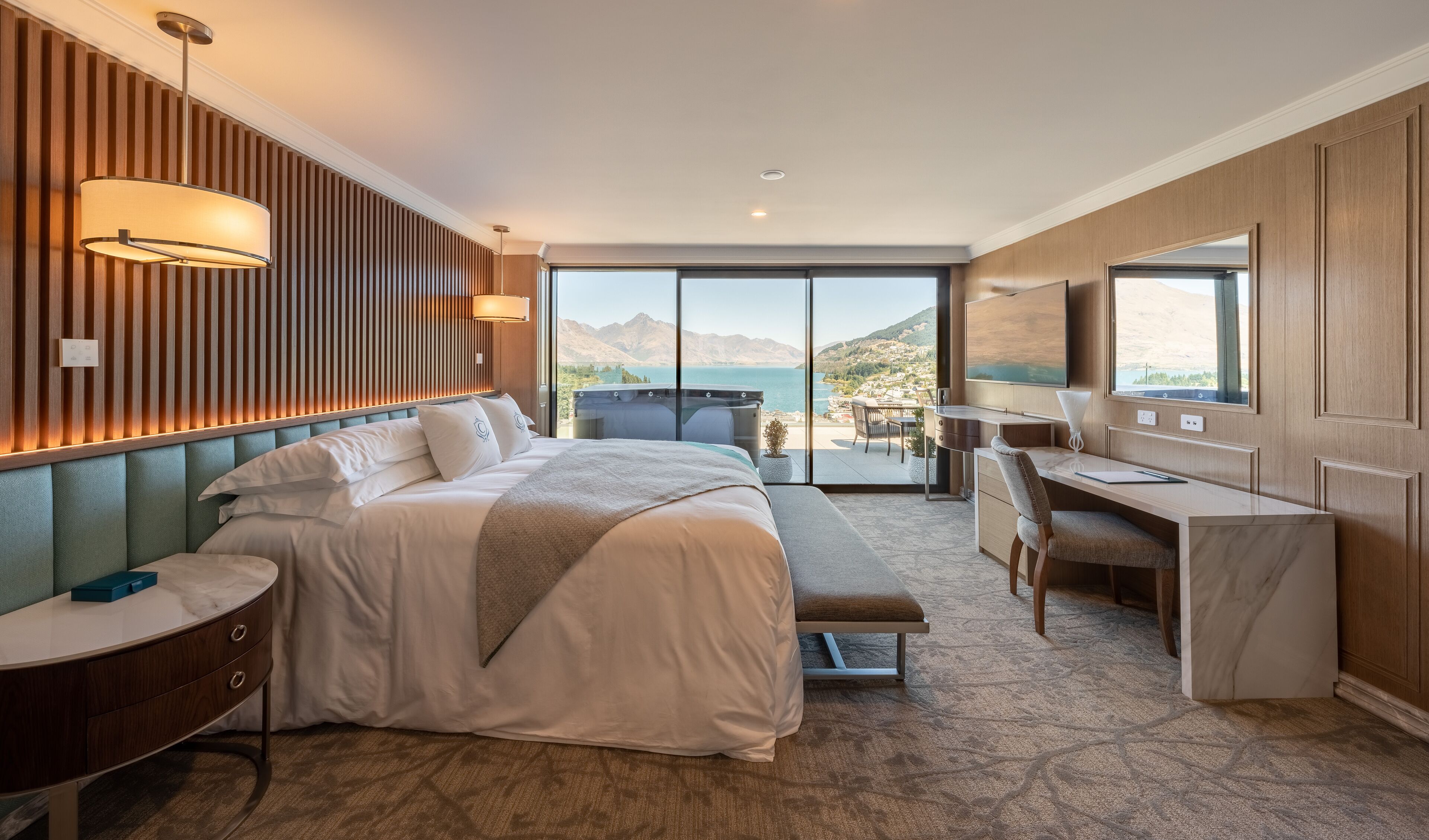 A hotel room with a bed, desk, and a view of the mountains and sea.