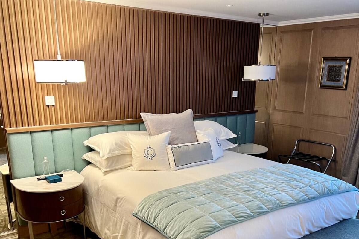 Een hotelkamer met een groot bed, een nachtkastje, een bankje, een wandlamp en een kamerkleed met dessin.